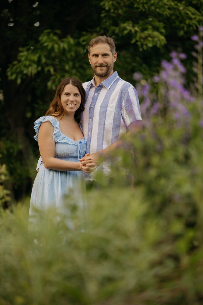 Couple standing together in a wildflower field, man in blue striped shirt