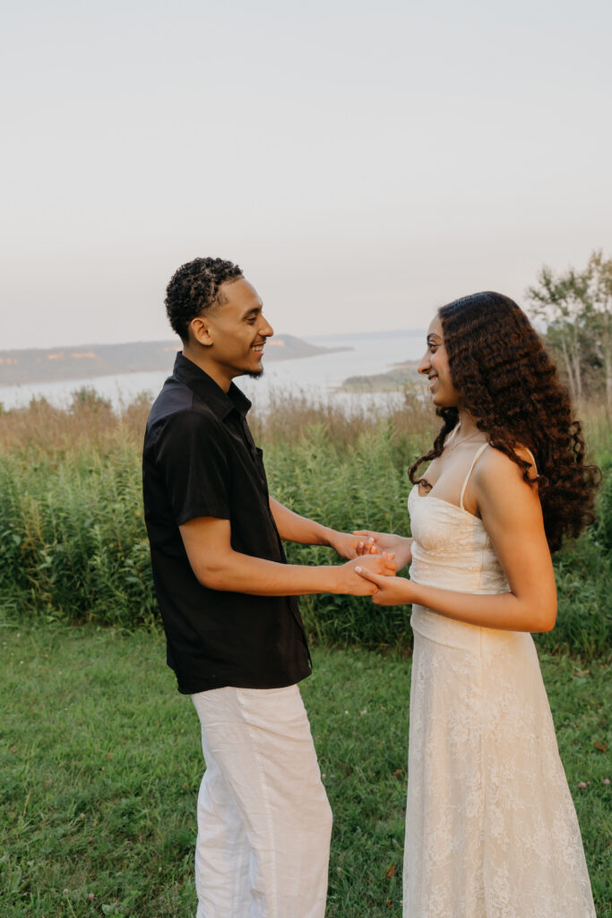 couple holding hands and smiling at each other after getting engaged near a lake