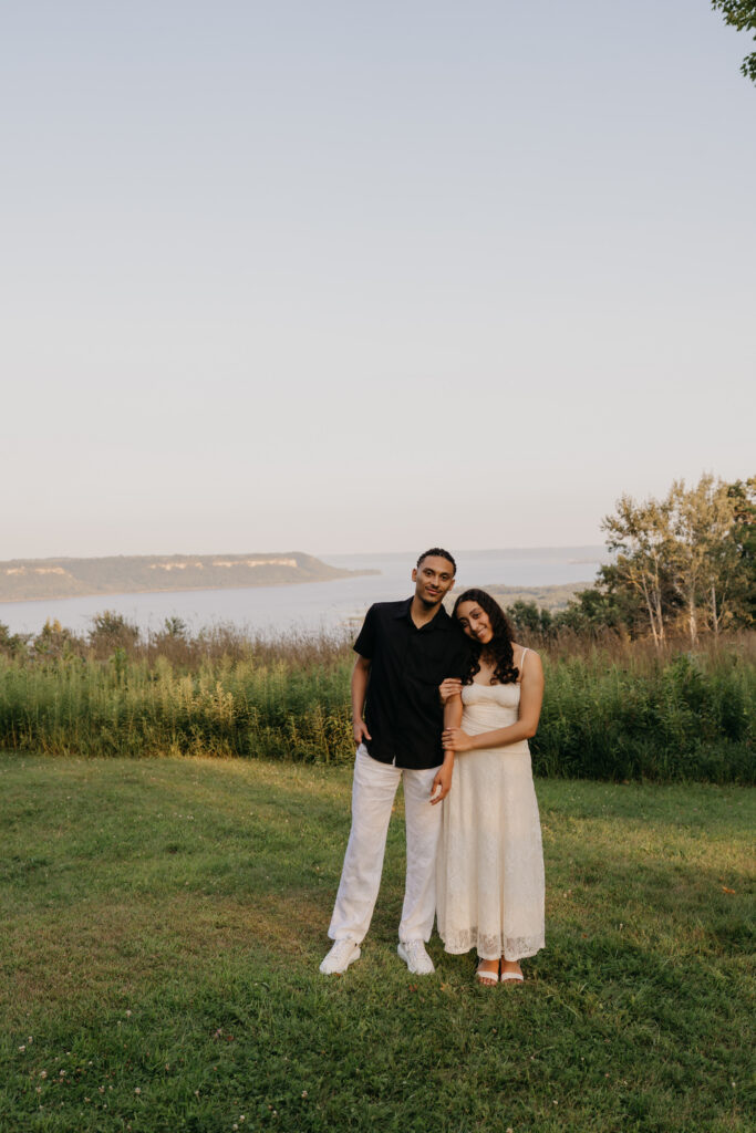 newly engaged couple standing together overlooking a lake at golden hour