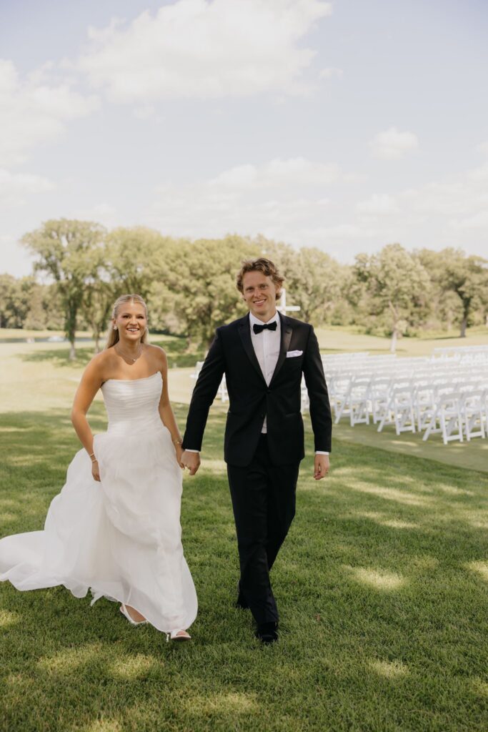 Bride and groom walking hand in hand toward outdoor ceremony chairs