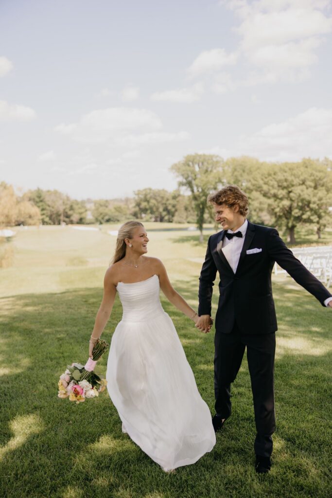Bride and groom walking across the lawn holding hands and bouquet