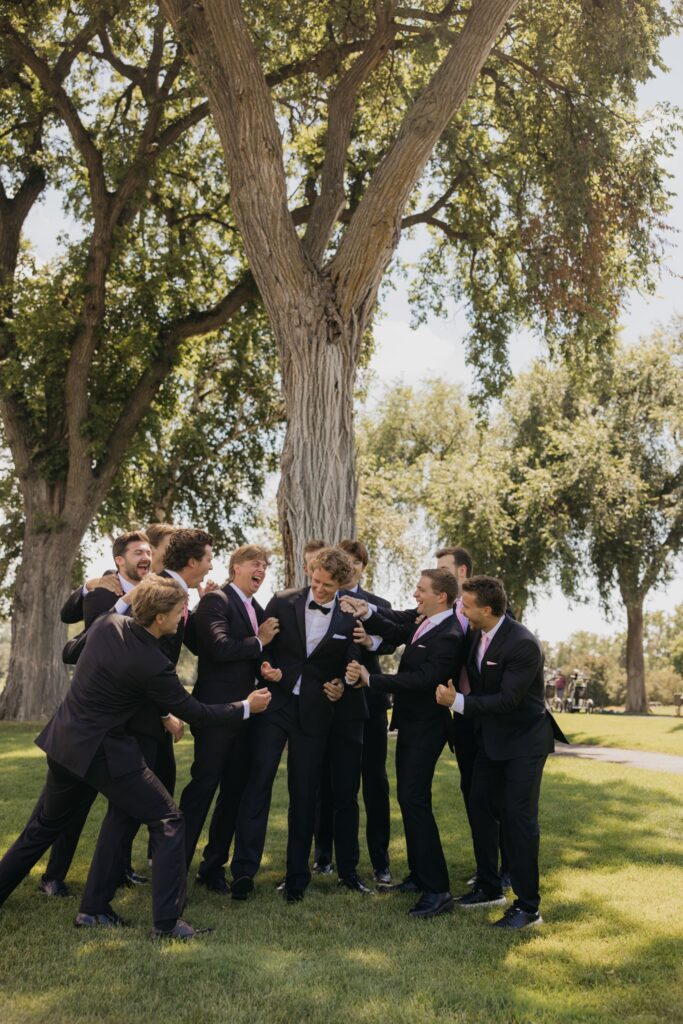 Groomsmen celebrating together under a large tree after the ceremony
