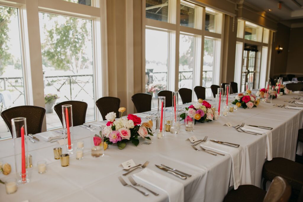 Reception table set with pink and white floral centerpieces and red taper candles