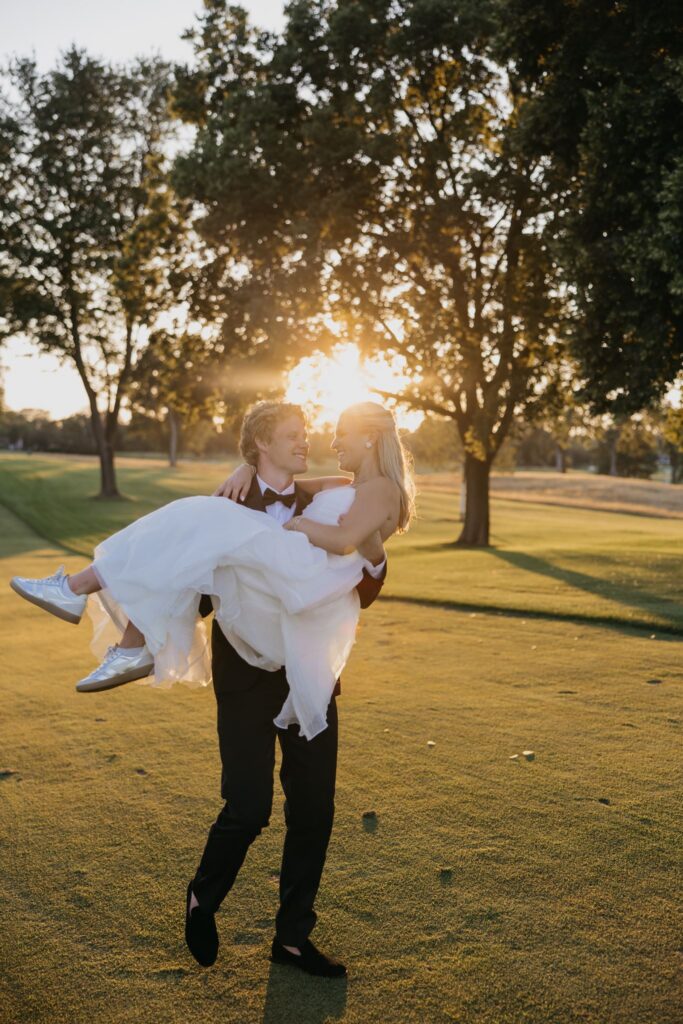 Groom carrying bride across the fairway during golden hour portraits