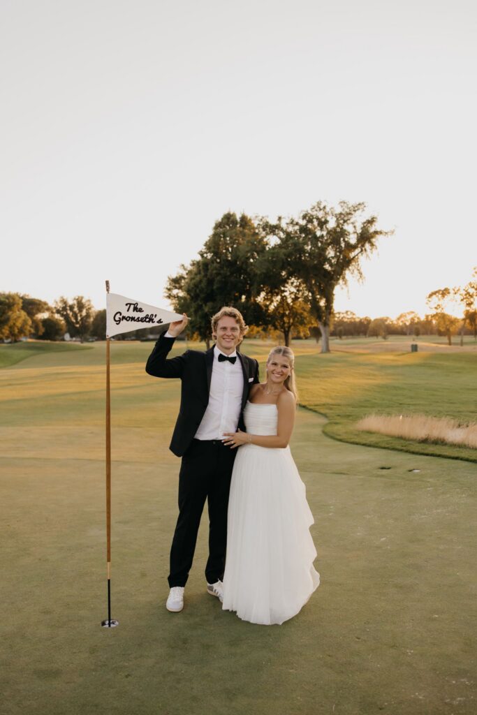 Bride and groom posing with a golf flag reading "The Gronseth's" on the putting green