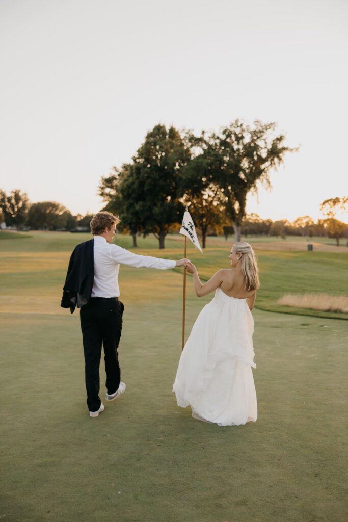 Bride and groom walking across the green holding a golf flag at Minneapolis Golf Club wedding