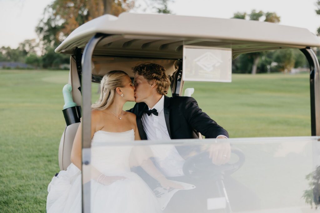 Bride and groom kissing while seated together in a golf cart