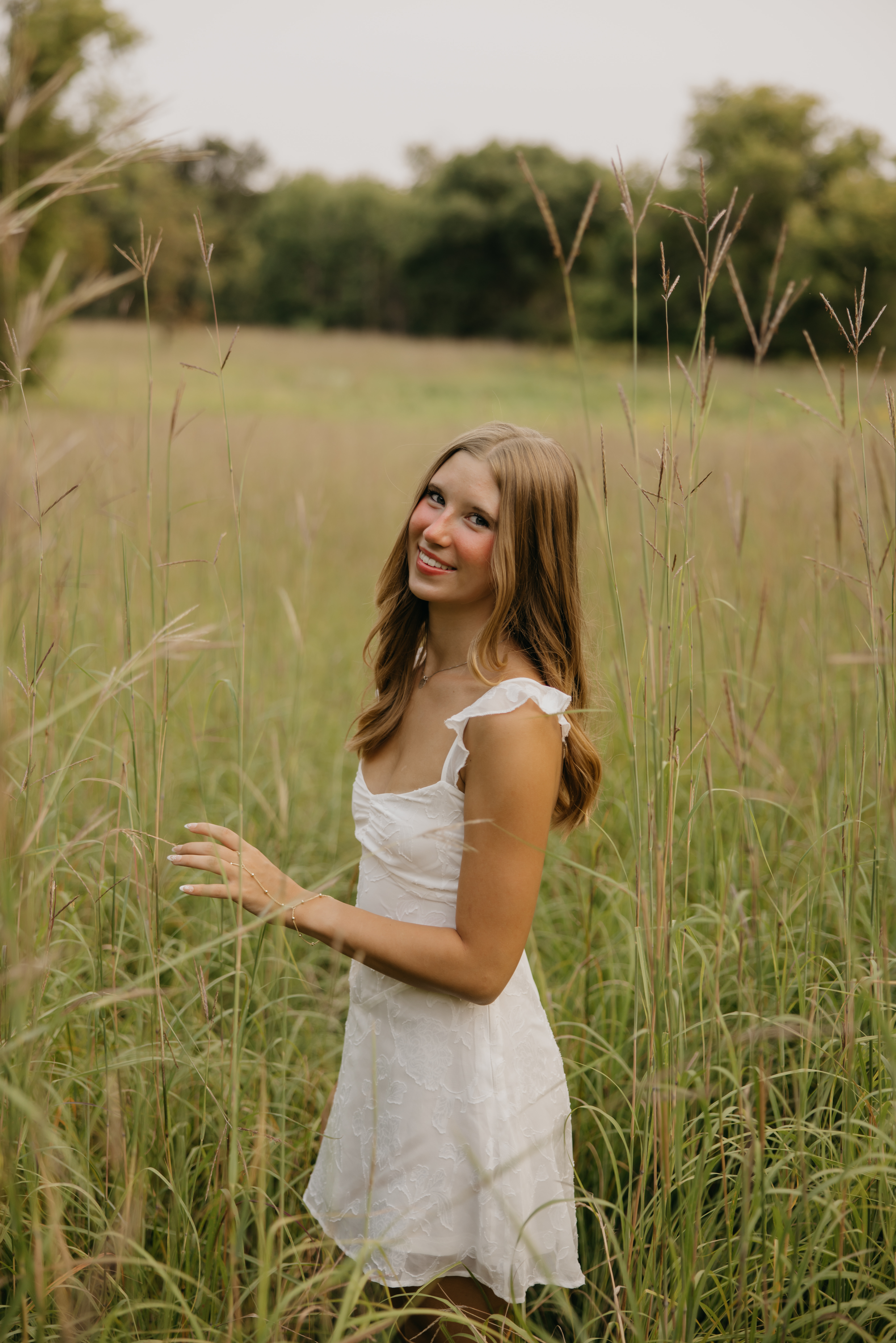 Senior Anya standing in tall prairie grass at Coldwater Spring, wearing a white dress