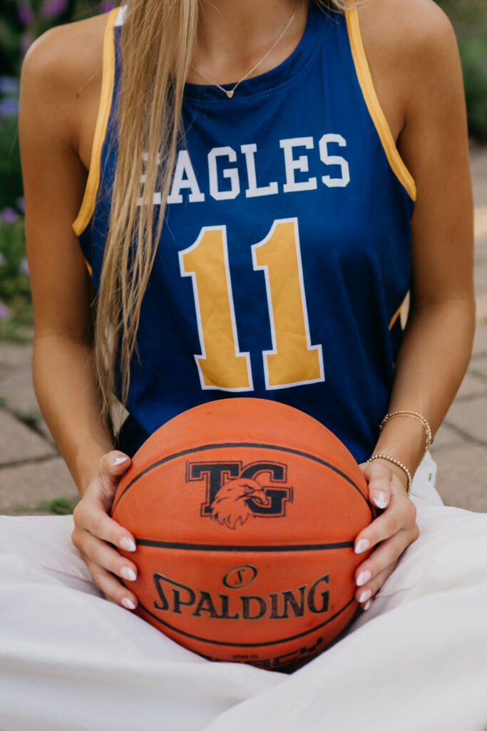 Close crop of senior girl in Eagles jersey number 11 holding a basketball at her waist