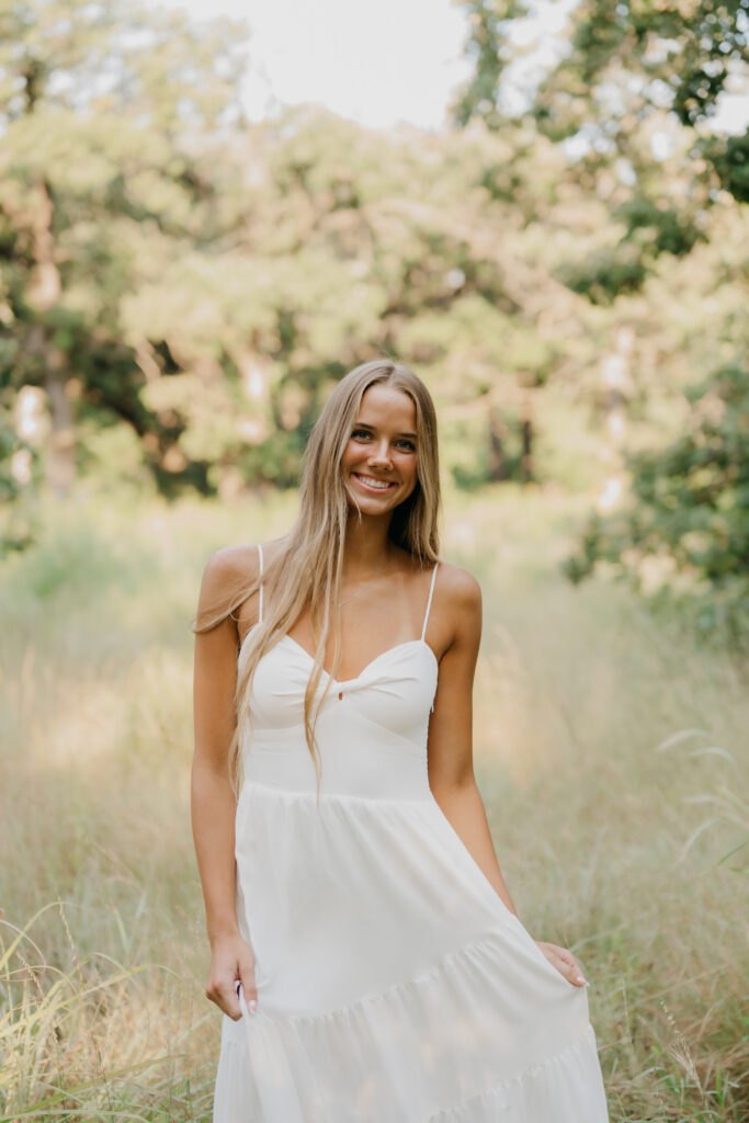 Senior girl in a flowing white tiered dress stands in a golden grass field