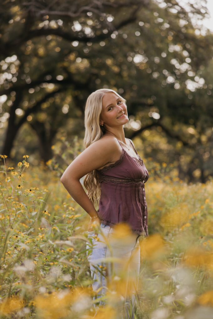 Senior girl standing in a wildflower field wearing a mauve top and jeans