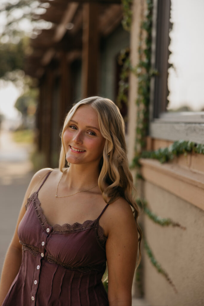 Senior girl standing near a building entrance smiling in a mauve top