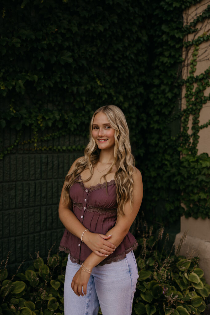 Senior girl standing against an ivy-covered stone wall in a mauve top