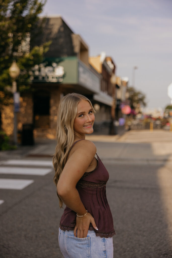 Senior girl standing on an urban sidewalk looking over her shoulder in a mauve top