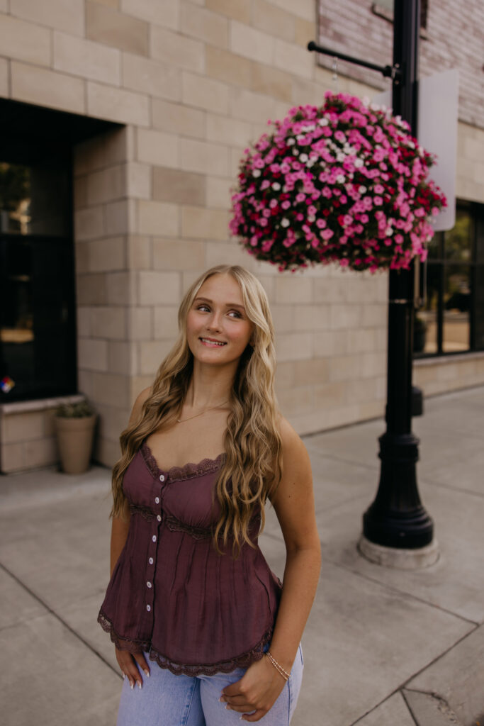 Senior girl standing under a hanging flower basket on a city sidewalk