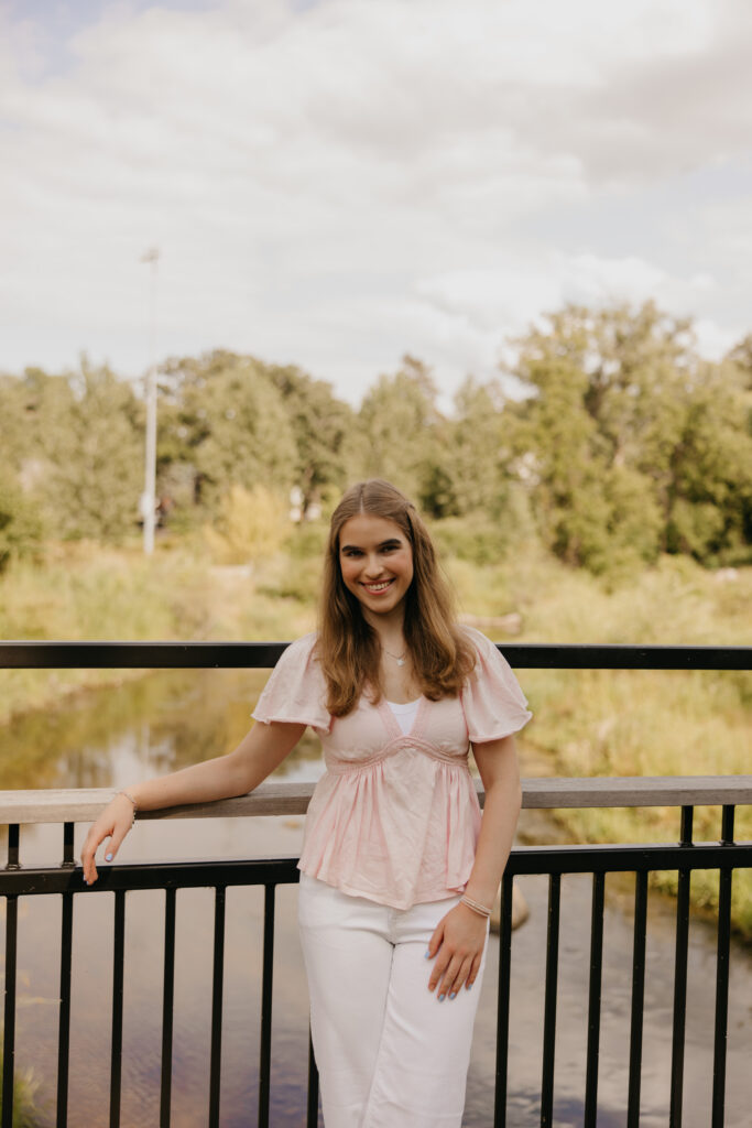Senior girl leaning on a black metal railing by the water in a pink top