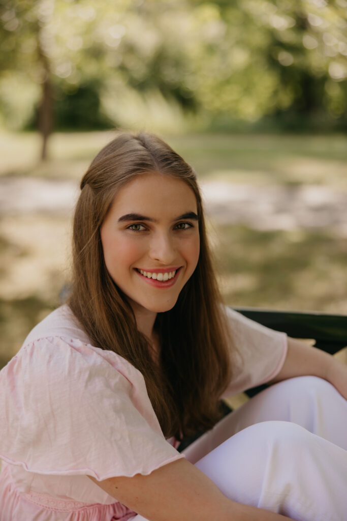 Senior girl smiling while sitting on a park bench in a pink top