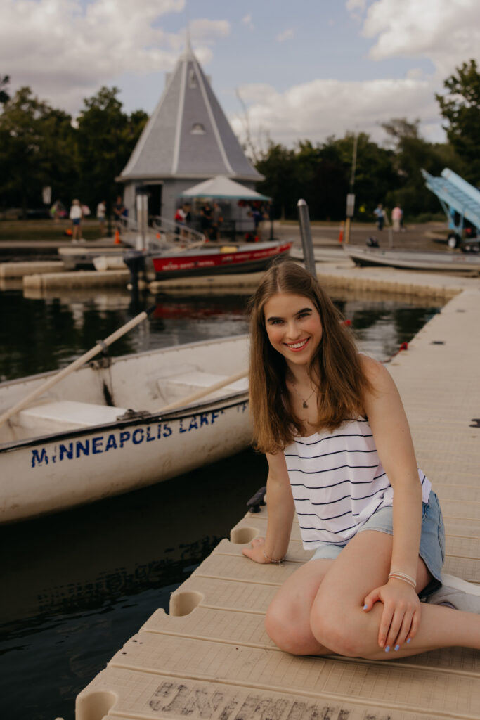 Senior girl sitting on a dock beside a boat labeled Minneapolis Lake