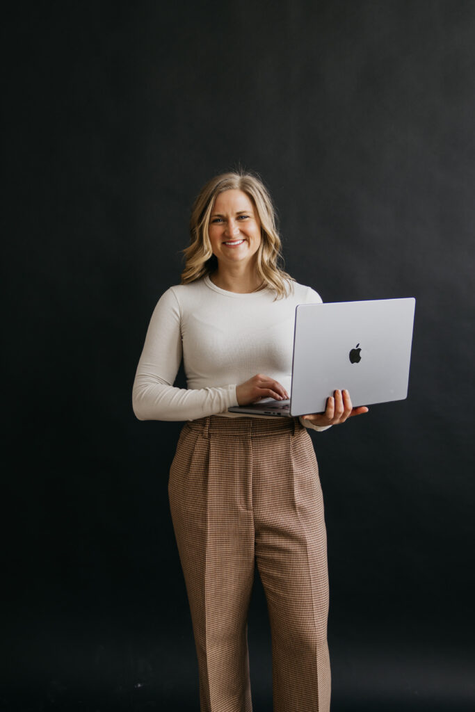 Callan Faulkner smiling and holding an open laptop while standing against a dark studio backdrop