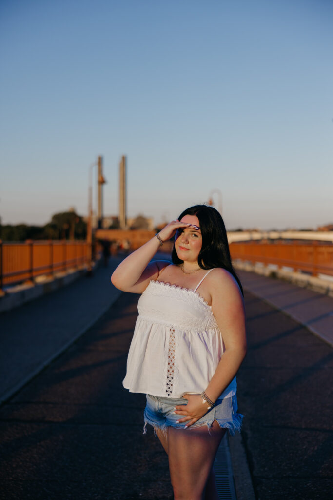 Senior girl shading her eyes on a bridge with industrial towers in the background