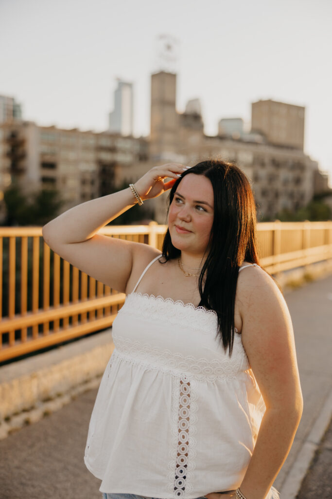 Senior girl shading her eyes on a bridge with the Minneapolis skyline behind her