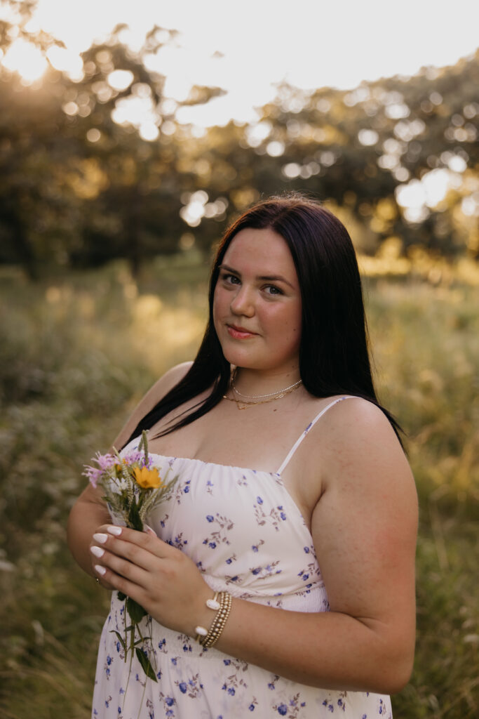 Senior girl in a white floral dress holding a small yellow wildflower