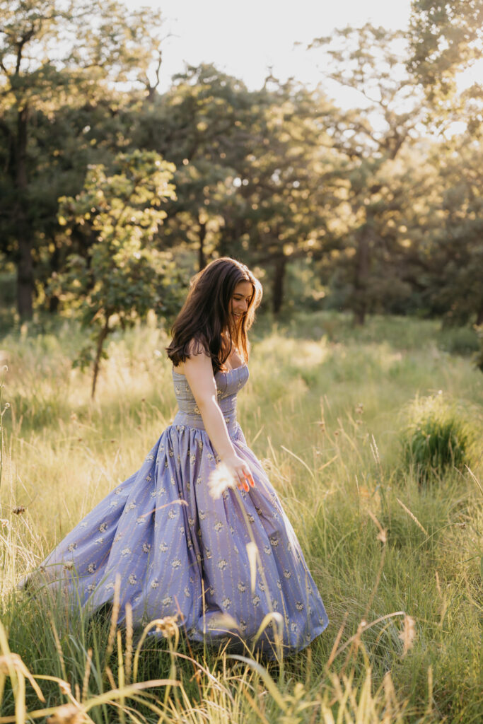 Emma Hollands standing in tall grass holding her blue floral dress