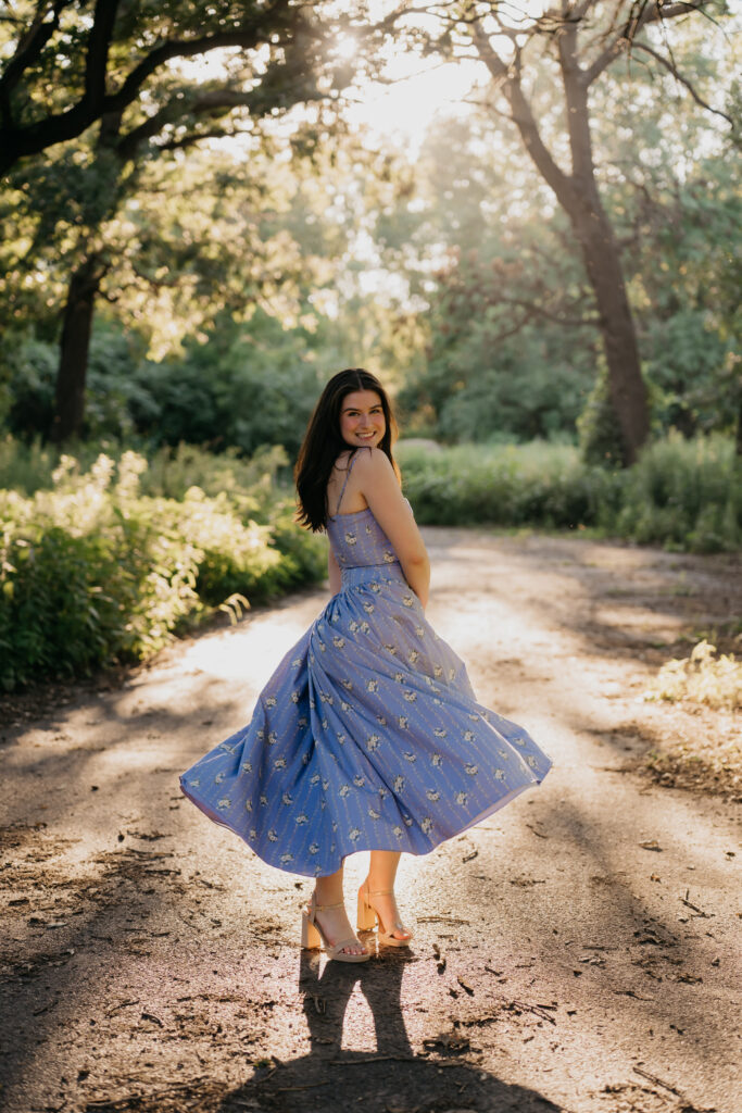Emma Hollands twirling in a blue floral dress on a wooded dirt path