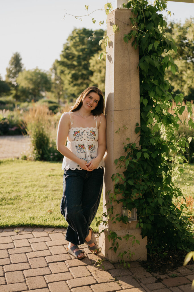 Senior leaning against a vine-covered pillar, wearing a white floral top