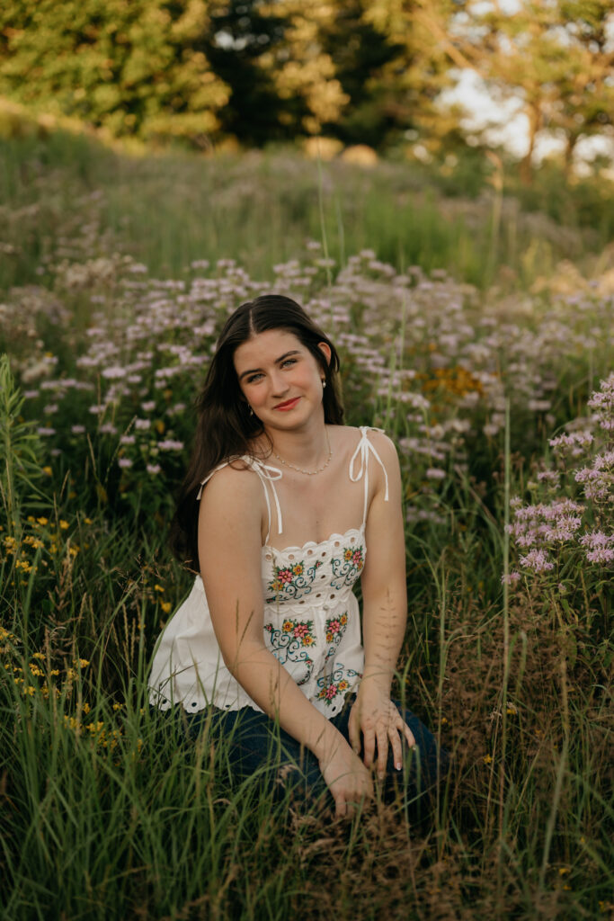 Emma Hollands sitting in a wildflower field in a white embroidered top