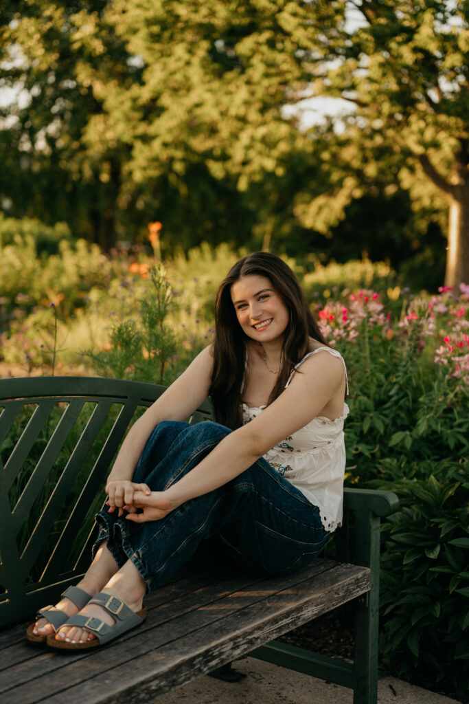 Senior sitting on a garden bench, wearing a white floral top and jeans