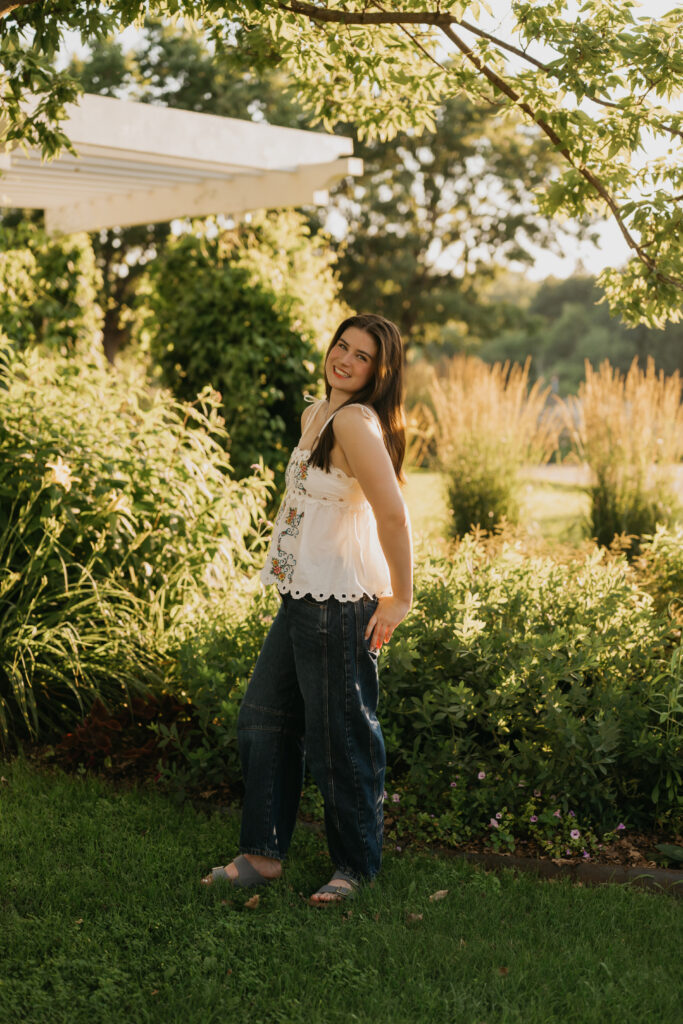 Senior standing on grass near tall ornamental grasses, wearing a white floral top