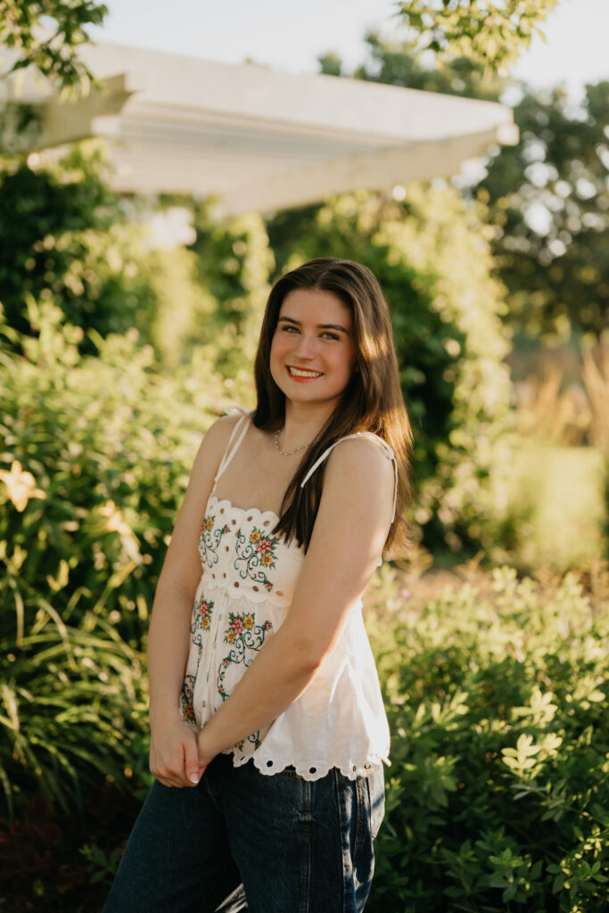 Emma Hollands standing under a garden structure in a white embroidered top