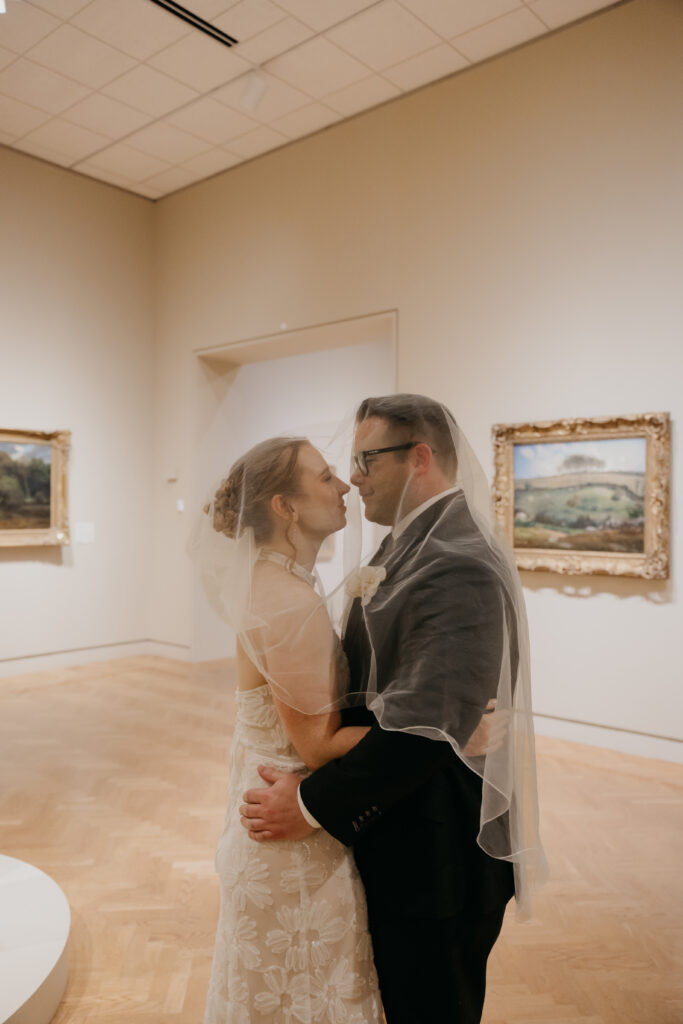 Bride and groom share an intimate moment under her veil in the gallery at their Minneapolis Institute of Art wedding