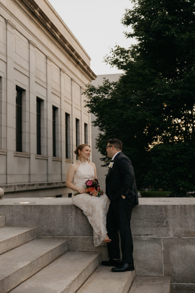 Bride and groom sit together on a stone ledge outside Mia at sunset
