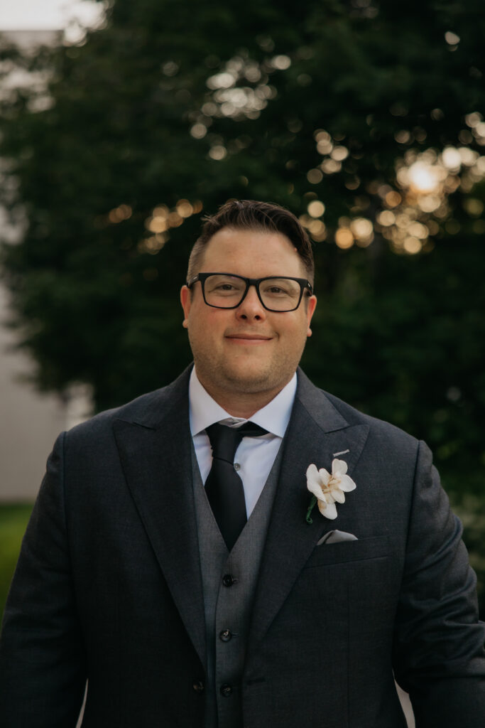 Groom portrait with boutonniere, trees and golden hour light behind him