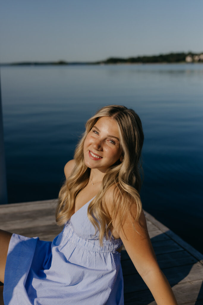 Eve sitting on the dock in a blue striped dress, lake behind her