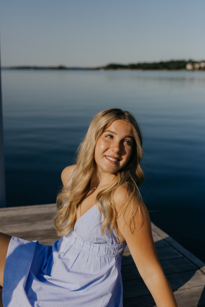 Senior Eve smiling over her shoulder on Wayzata Docks in a blue striped dress