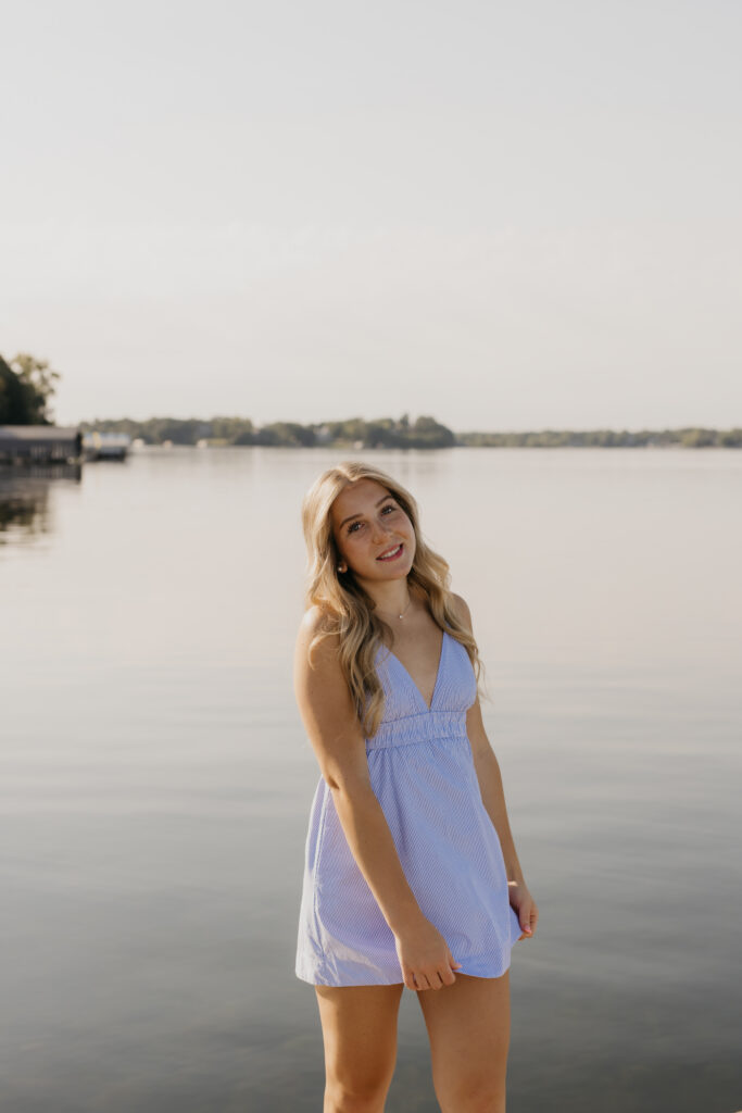 Senior Eve standing on Wayzata Docks in a blue striped dress, looking out at the lake
