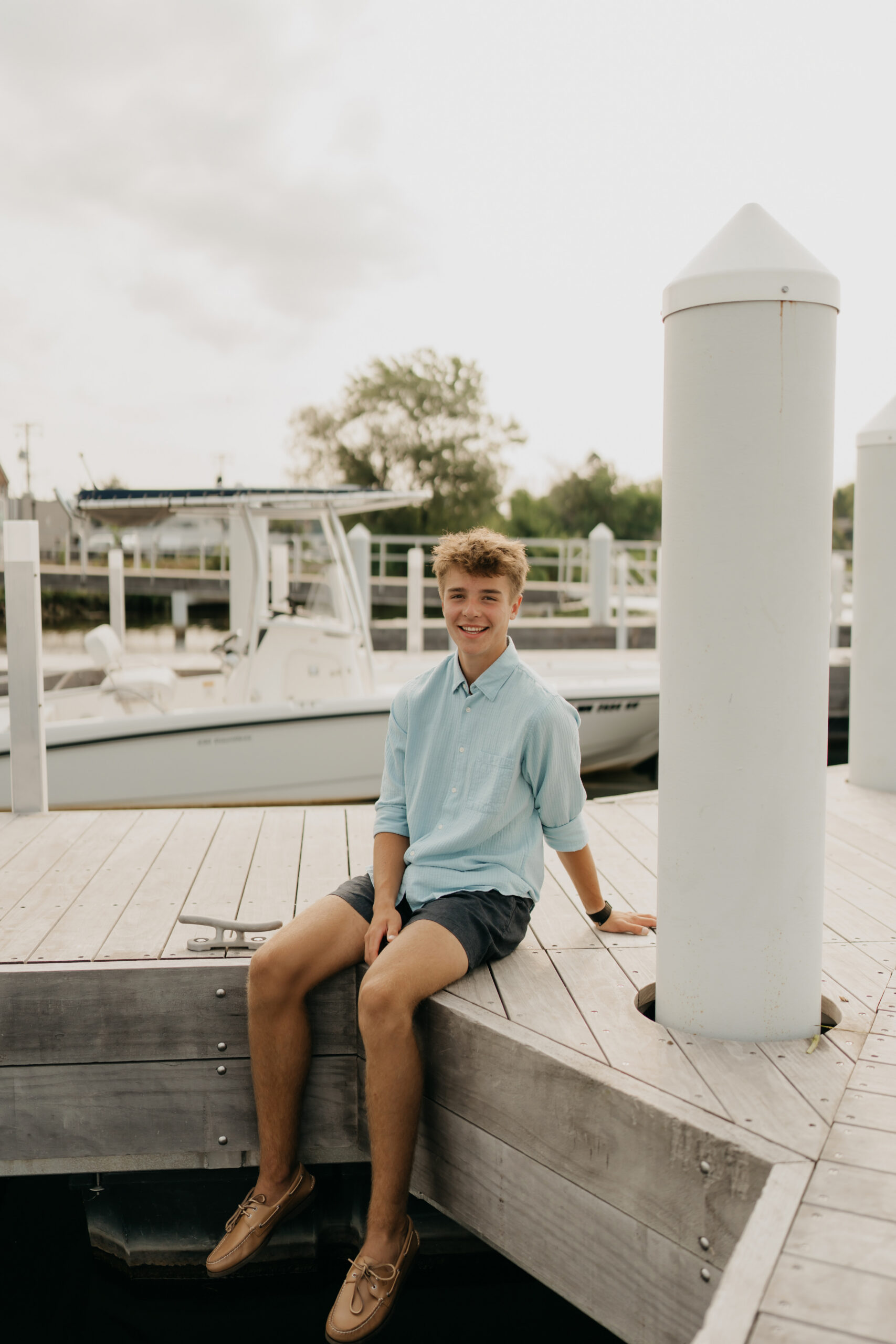 Senior Grant sitting on the edge of Wayzata Docks with boats and marina in the background