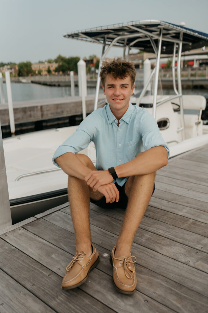 Senior Grant sitting cross-legged on Wayzata Docks beside a docked boat