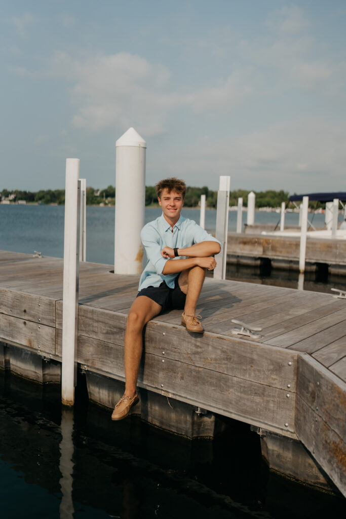 Grant sitting on the edge of the dock, in a light blue shirt and shorts