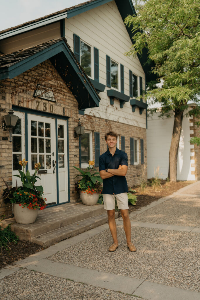 Grant standing outside a brick building with blue trim, in a light blue shirt and shorts