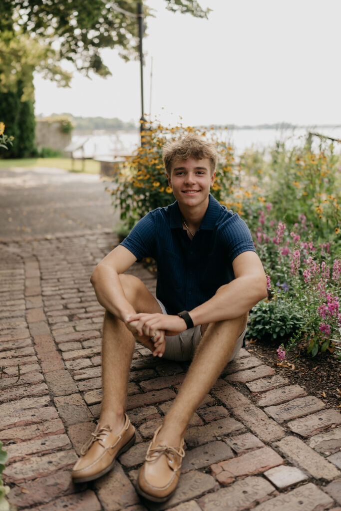 Grant sitting on a brick path near the water, in a navy shirt and shorts