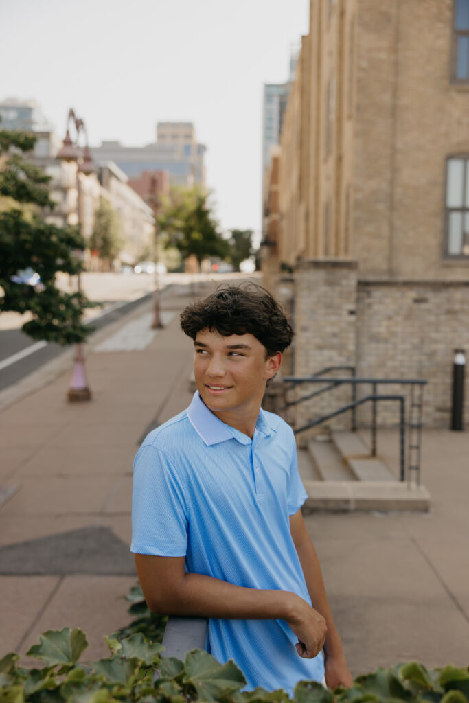 Senior in light blue polo standing on a downtown Minneapolis street with brick buildings behind him