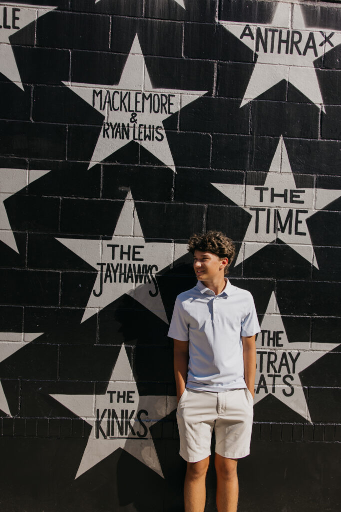 Senior in light blue polo standing in profile with hands in pockets in front of the star mural
