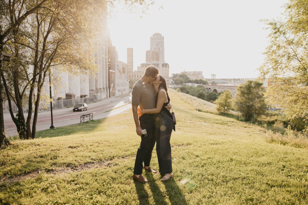 newly engaged couple embracing on a grassy hill overlooking the city skyline