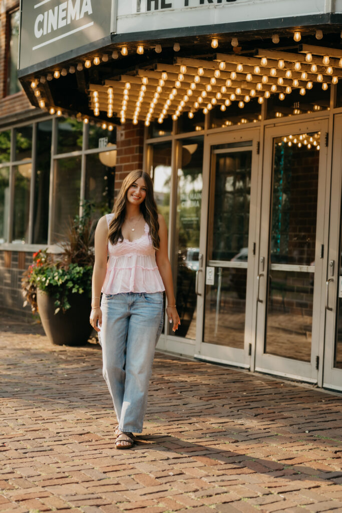 Senior girl in pink lace top walking past theater marquee lights at St. Anthony Main