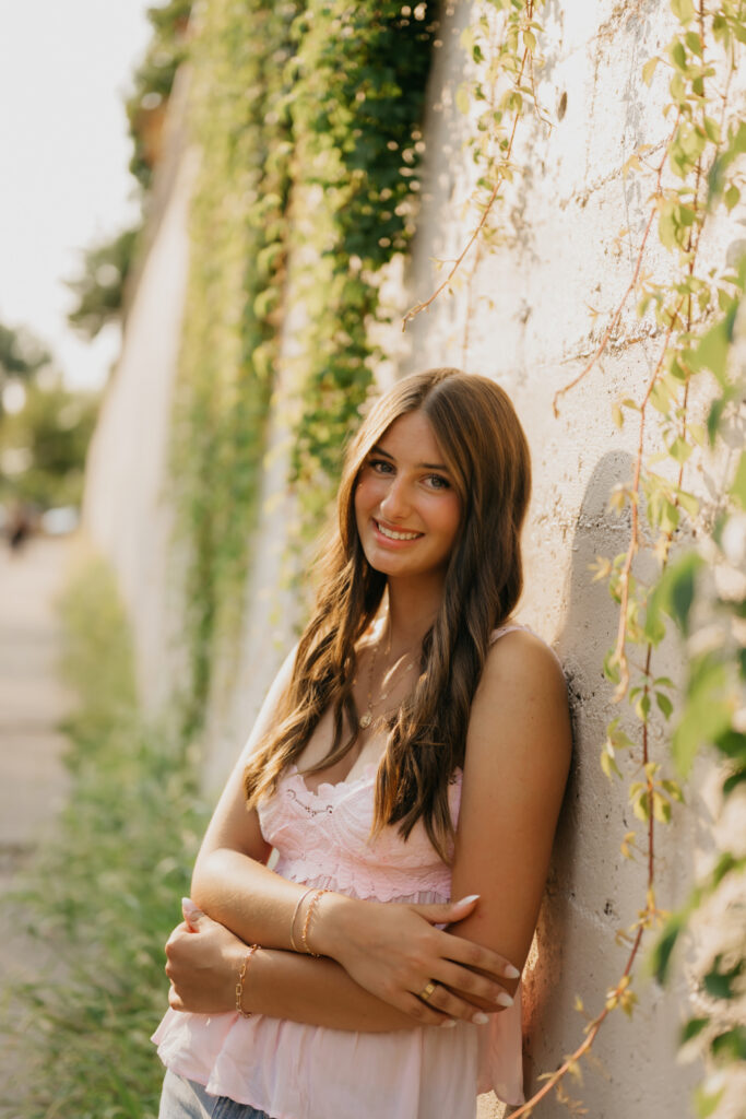Senior girl in pink lace top leaning against ivy-covered wall at St. Anthony Main