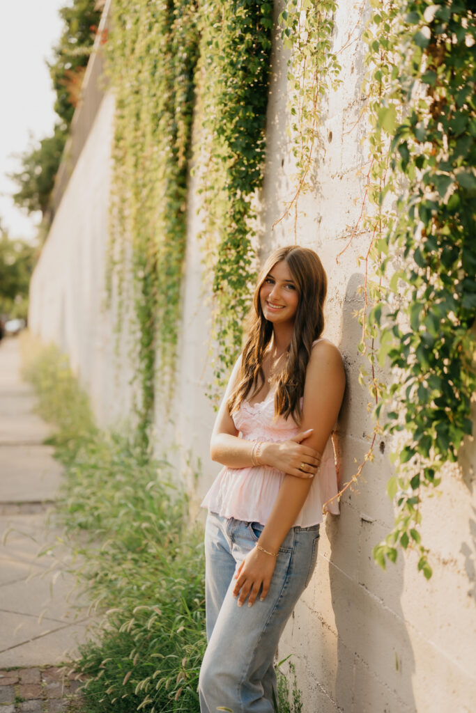 Senior girl in pink lace top leaning against ivy-covered wall at St. Anthony Main
